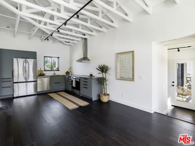 kitchen featuring stainless steel appliances, wall chimney exhaust hood, dark wood-type flooring, and high vaulted ceiling