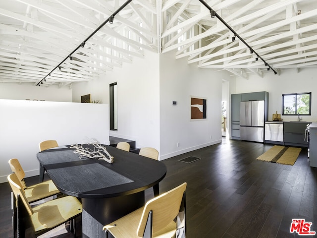 dining area with a towering ceiling, rail lighting, sink, and dark hardwood / wood-style flooring