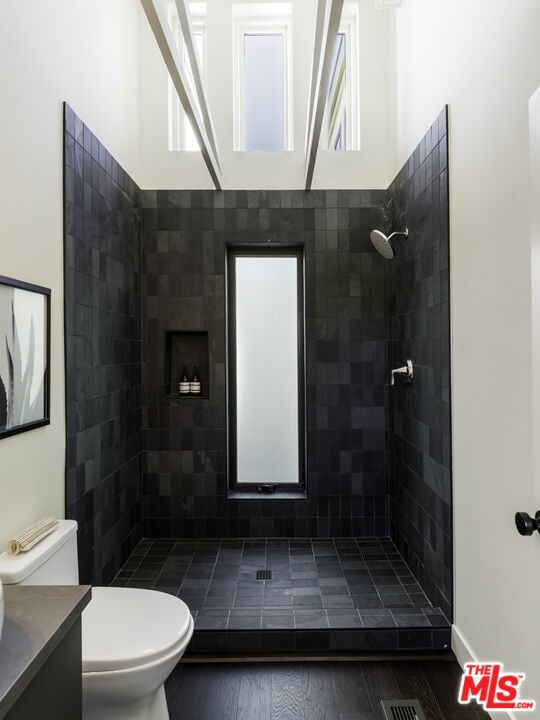 bathroom featuring tiled shower, hardwood / wood-style floors, vanity, and toilet