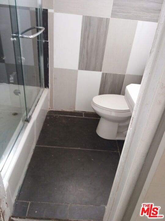 bathroom with tile flooring, combined bath / shower with glass door, and toilet