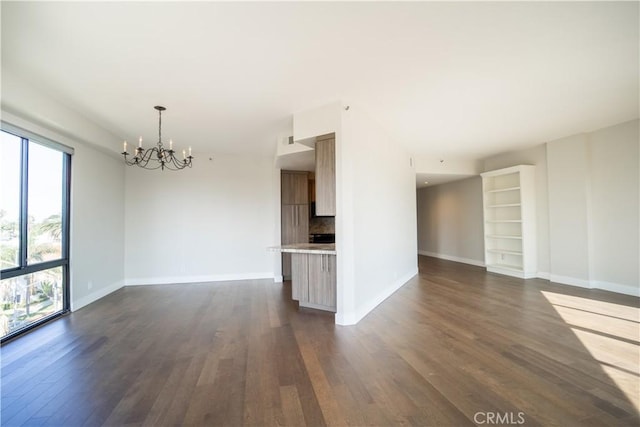 empty room featuring built in shelves, dark hardwood / wood-style flooring, and a notable chandelier