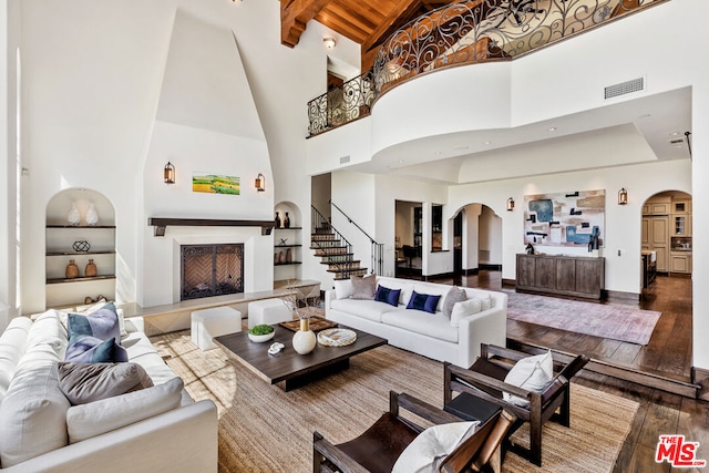 living room featuring beam ceiling, built in shelves, a high ceiling, and hardwood / wood-style flooring