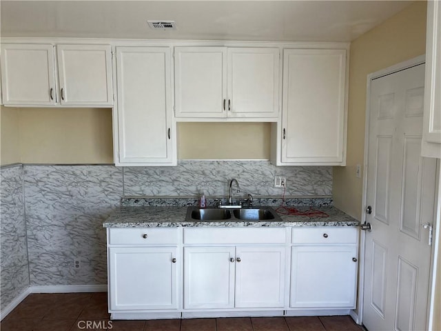 kitchen with sink, tasteful backsplash, dark tile patterned floors, dark stone counters, and white cabinets