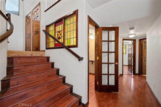 stairs featuring hardwood / wood-style floors, a textured ceiling, vaulted ceiling, and french doors