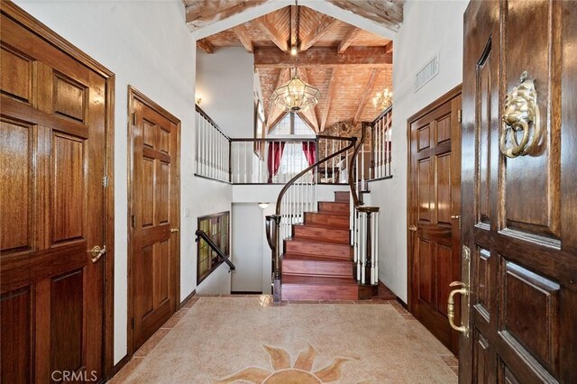 foyer with a towering ceiling, wood ceiling, light colored carpet, beam ceiling, and a chandelier