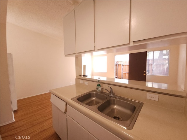 kitchen with sink, white cabinets, a textured ceiling, and light wood-type flooring