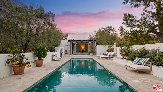 pool at dusk with a patio and a pergola