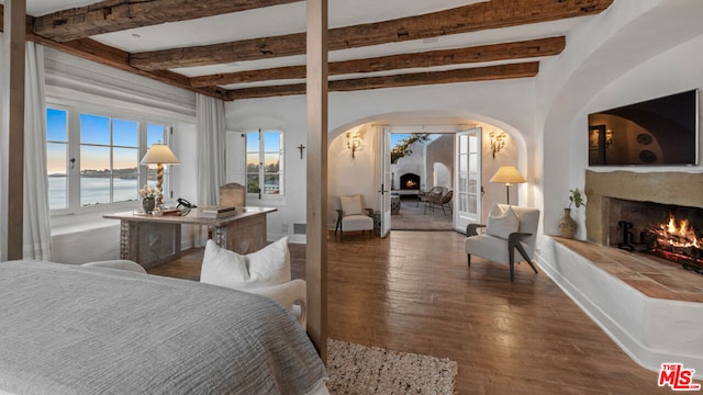 bedroom featuring a water view, a fireplace, dark hardwood / wood-style flooring, and beamed ceiling