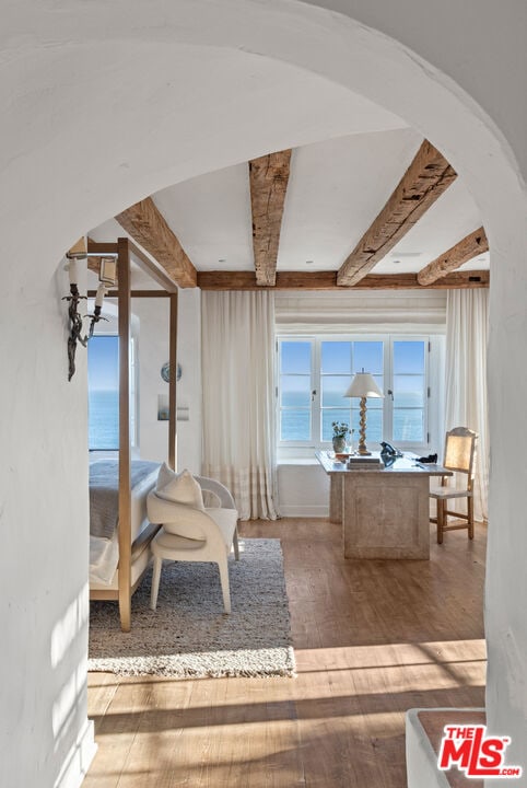 bedroom with beam ceiling, a water view, and hardwood / wood-style flooring