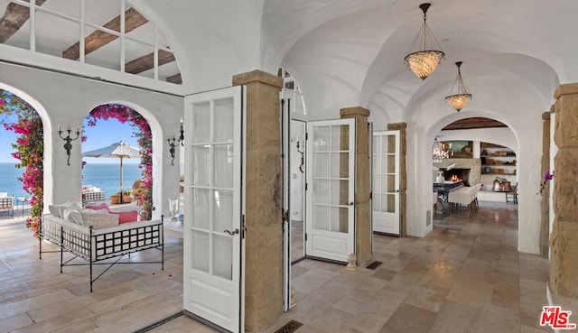 corridor with tile flooring, a water view, built in shelves, french doors, and ornate columns