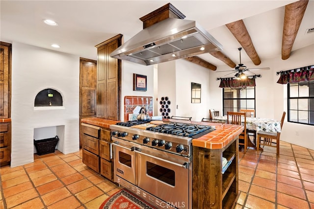 kitchen featuring range with two ovens, tile counters, island exhaust hood, beam ceiling, and light tile floors