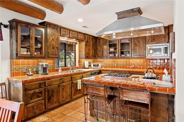 kitchen featuring island exhaust hood, tasteful backsplash, appliances with stainless steel finishes, sink, and tile countertops