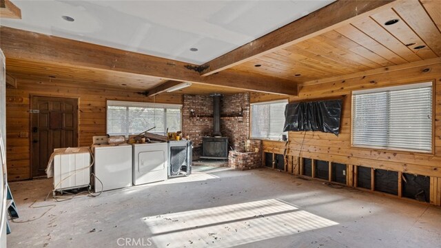 misc room featuring washing machine and dryer, beam ceiling, a wood stove, and wood walls