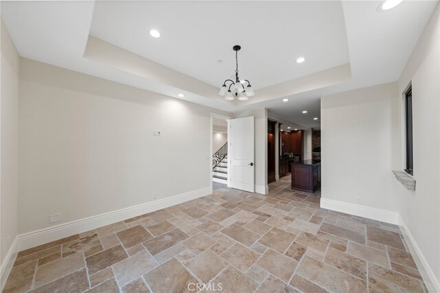 unfurnished room featuring a notable chandelier, light tile floors, and a raised ceiling