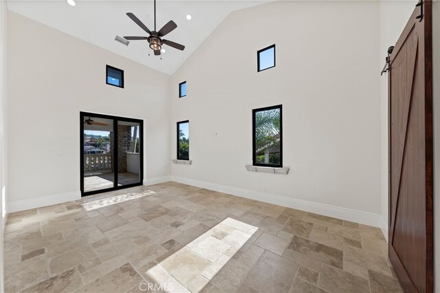 empty room featuring a barn door, ceiling fan, high vaulted ceiling, and light tile flooring