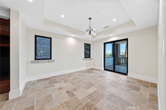 tiled empty room featuring a tray ceiling and an inviting chandelier