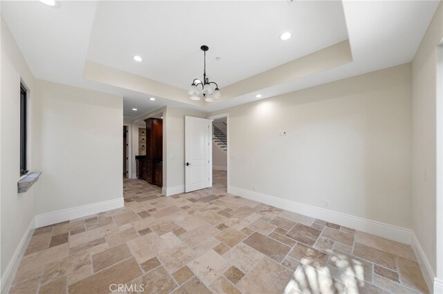 tiled spare room featuring a notable chandelier and a tray ceiling