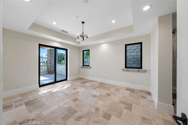 spare room with a chandelier, a raised ceiling, and light tile flooring