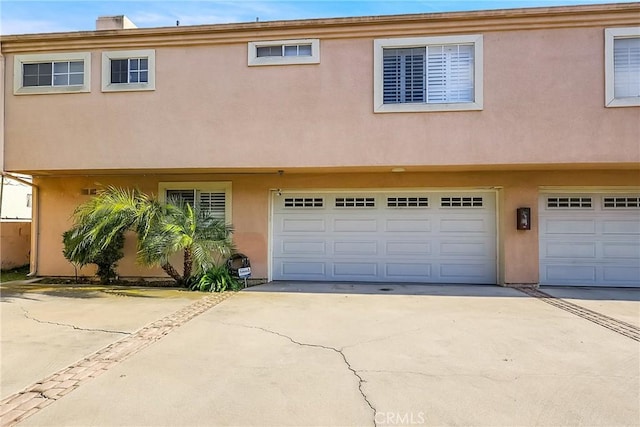 townhome / multi-family property with an attached garage, a chimney, concrete driveway, and stucco siding