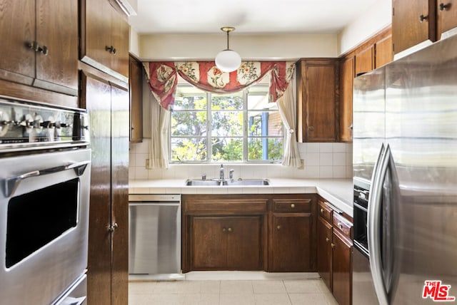 kitchen featuring appliances with stainless steel finishes, backsplash, decorative light fixtures, and sink