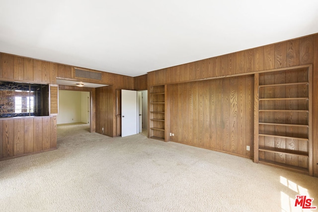 unfurnished living room featuring wood walls and light carpet