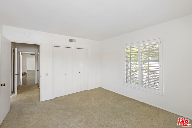 unfurnished bedroom with light colored carpet and a closet