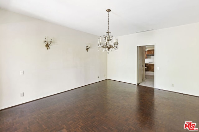 spare room with dark parquet floors and an inviting chandelier