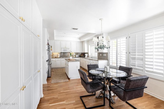 dining room featuring a tray ceiling, sink, a chandelier, and light wood-type flooring