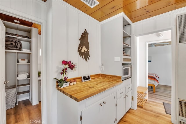 kitchen featuring wood ceiling, wooden walls, white cabinetry, light wood-type flooring, and crown molding