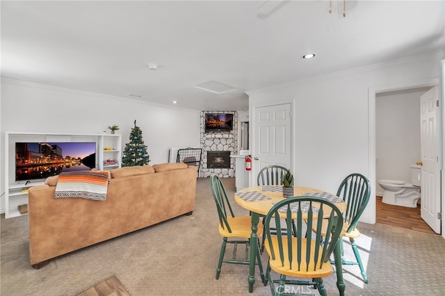 dining room featuring a stone fireplace, ornamental molding, and carpet