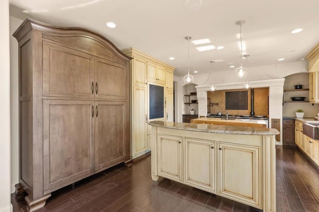 kitchen with light stone countertops, pendant lighting, dark hardwood / wood-style flooring, and a kitchen island with sink