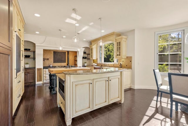 kitchen featuring decorative backsplash, light stone counters, pendant lighting, dark hardwood / wood-style floors, and an island with sink