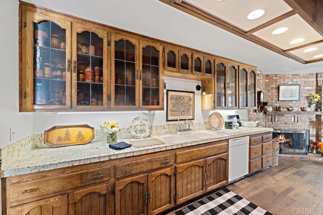 kitchen with glass insert cabinets, light countertops, wood finished floors, white dishwasher, and a sink