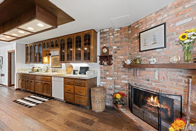 kitchen featuring brown cabinets, dark wood-type flooring, a fireplace, white dishwasher, and light countertops