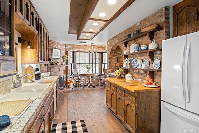 kitchen with a sink, freestanding refrigerator, brick wall, glass insert cabinets, and wood-type flooring