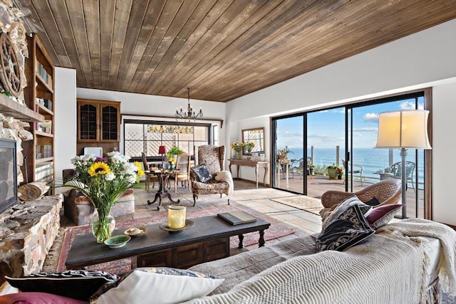 living room with a notable chandelier, a stone fireplace, a water view, and plenty of natural light