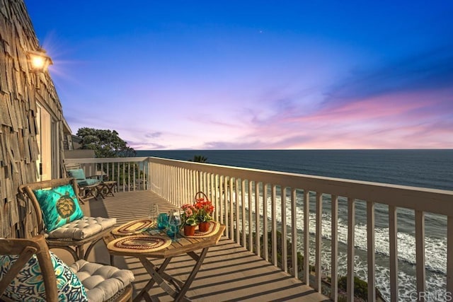 balcony at dusk featuring a view of the beach and a water view