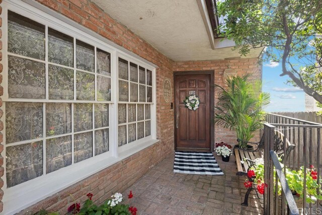 view of exterior entry featuring brick siding and fence