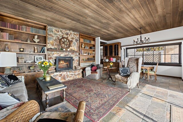 living area with stone tile floors, a stone fireplace, baseboards, built in shelves, and a notable chandelier