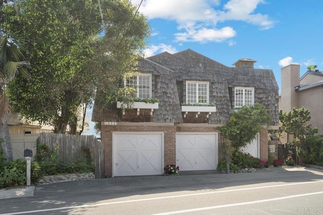 view of front facade with brick siding, an attached garage, mansard roof, and fence
