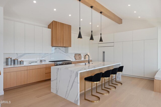 kitchen featuring decorative light fixtures, white cabinets, light hardwood / wood-style flooring, backsplash, and an island with sink