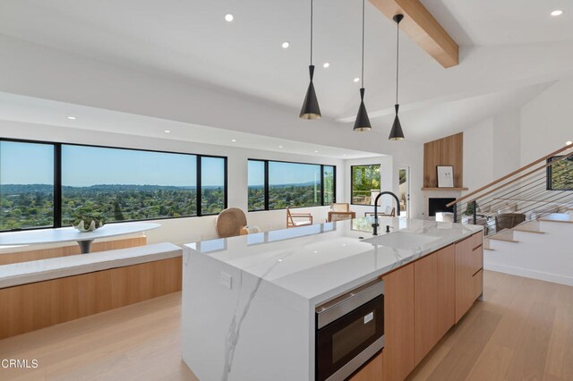 kitchen with sink, stainless steel microwave, decorative light fixtures, a large island with sink, and light stone countertops