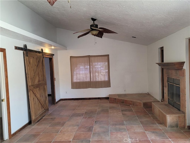 unfurnished living room with a textured ceiling, ceiling fan, a tile fireplace, a barn door, and lofted ceiling