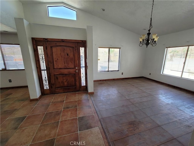 foyer with a chandelier, dark tile patterned flooring, vaulted ceiling, and a healthy amount of sunlight