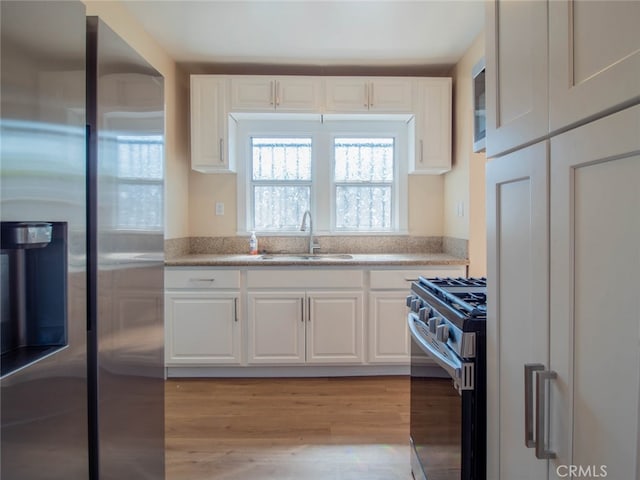 kitchen with white cabinetry, sink, light hardwood / wood-style floors, and appliances with stainless steel finishes