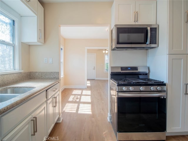 kitchen featuring ceiling fan, light stone countertops, light hardwood / wood-style flooring, white cabinets, and appliances with stainless steel finishes