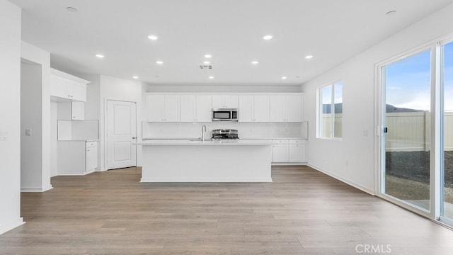 kitchen featuring a kitchen island with sink, white cabinetry, light hardwood / wood-style floors, and appliances with stainless steel finishes