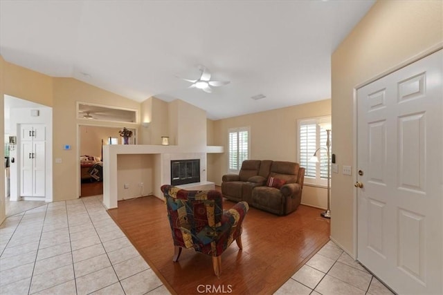 living room featuring light tile patterned floors, lofted ceiling, a ceiling fan, and a tiled fireplace