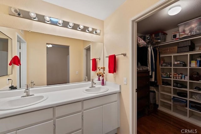 full bath with a sink, a walk in closet, wood finished floors, and double vanity