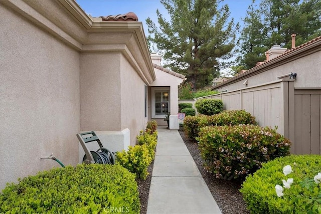 doorway to property with stucco siding, a tile roof, and fence